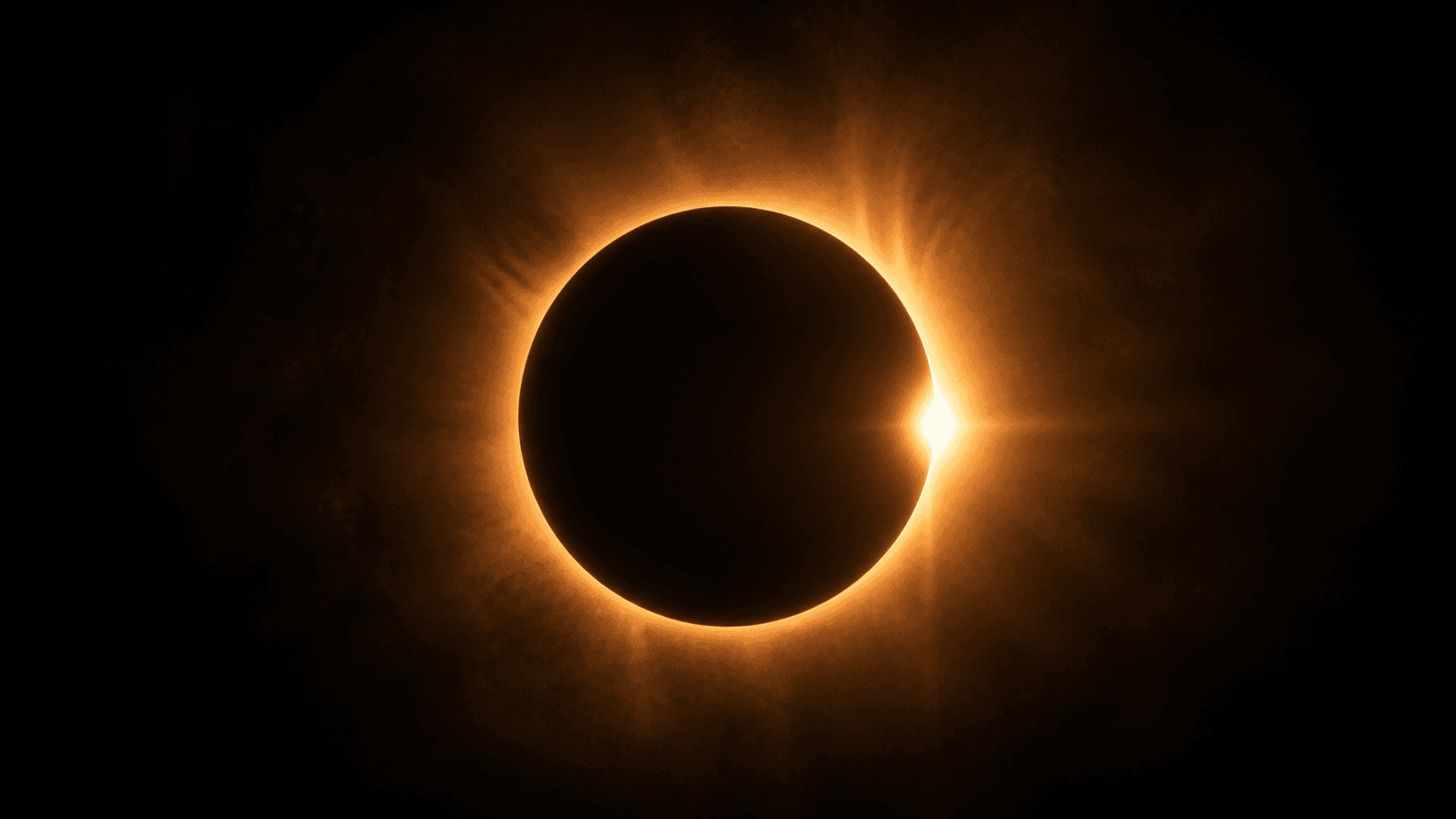 A solar eclipse with an amber corona and diamond-ring flare